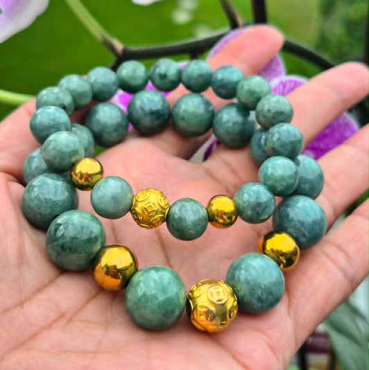 Hand holding a green Burmese Jadeite Jade bracelet with gold silver Beads in front of pink orchids.