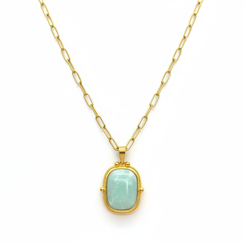 A gold pendant necklace with a light green stone, displayed on a textured white jewelry cushion.