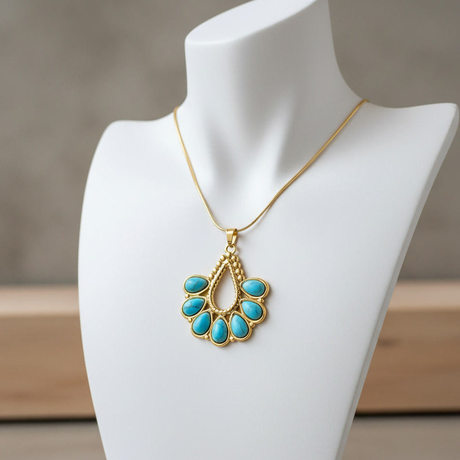 Gold pendant necklace with turquoise-colored oval stones, displayed on a white jewelry bust against a soft neutral background. The brand name 'AUREA JEWELS' is visible in the bottom right corner.